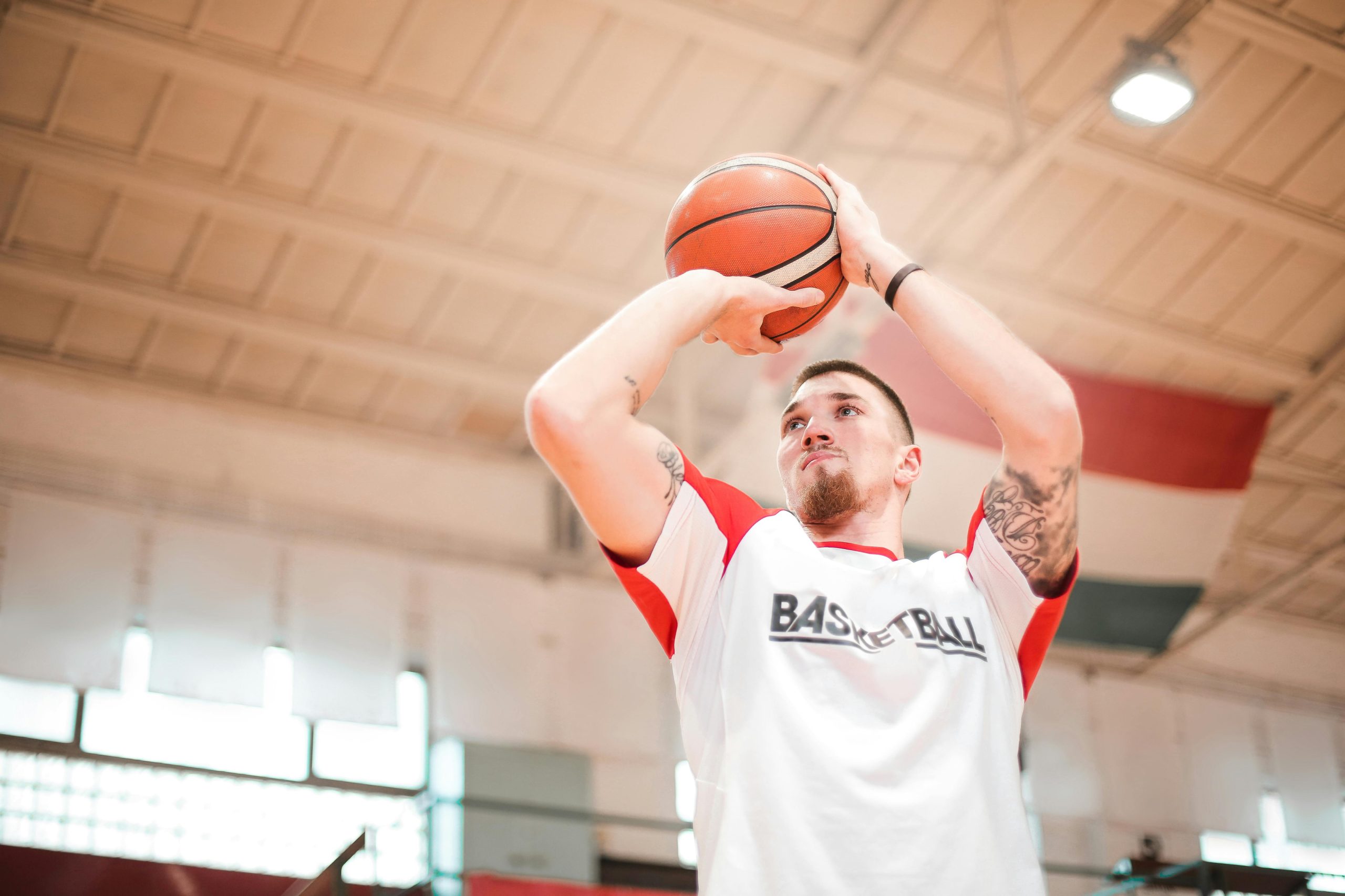 From below of concentrated basketball player with tattoos on arms preparing throwing ball to hoop